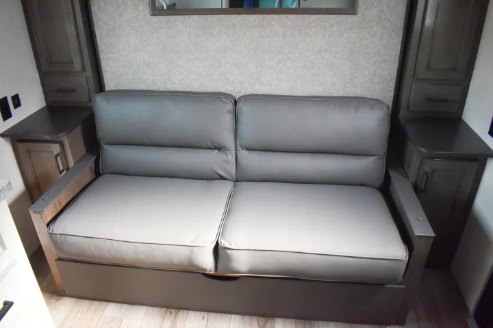 Cozy grey pull-out RV sofa bed, flanked by wood cabinets, in a modern RV rental. Compact living comfort.. Open Range 20MB 2021