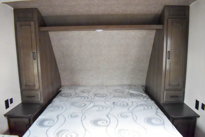 Cozy RV bedroom features a bed, two storage cabinets, and overhead shelving, ideal for your next rv rental trip.. Open Range 20MB 2021