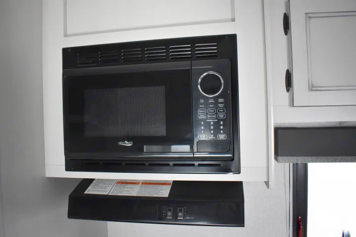 This RV rental kitchen features a black High Pointe microwave and Heng's range hood under white cabinets.. Open Range 20MB 2021