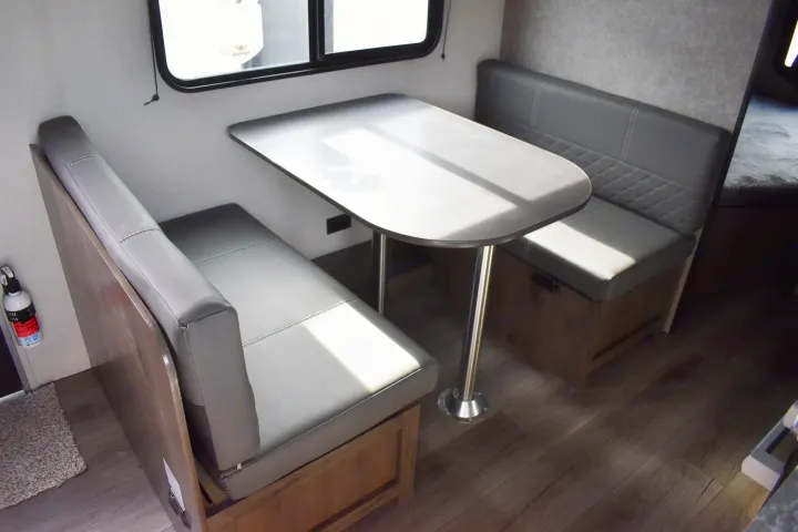 Light-filled RV rental dinette features grey cushioned benches and a table by the window, ideal for camper meals.. Open Range 20MB 2021