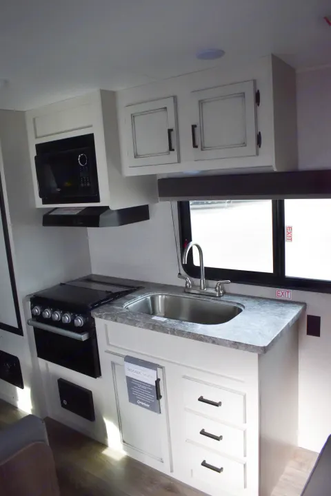Compact RV rental kitchen featuring a stove, microwave, sink, and ample cabinets, perfect for travel.. Open Range 20MB 2021