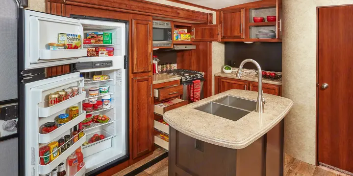 This rv rental kitchen showcases a large, open refrigerator, microwave, stove, and ample pull-out pantry storage.. Jayco Eagle HT 2018