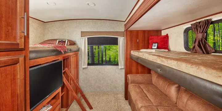 Spacious RV rental interior with bunk beds, TV, and a sofa, offering a cozy travel experience with forest views.. Jayco Eagle HT 2018