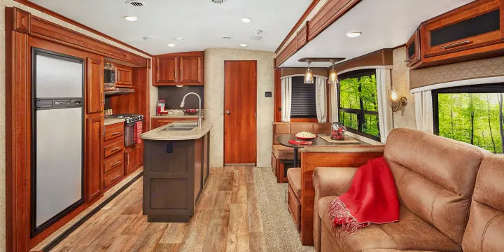 Inside an RV rental: a well-equipped kitchen, dining booth, and comfy sofa. Large windows show a lush forest.. Jayco Eagle HT 2018