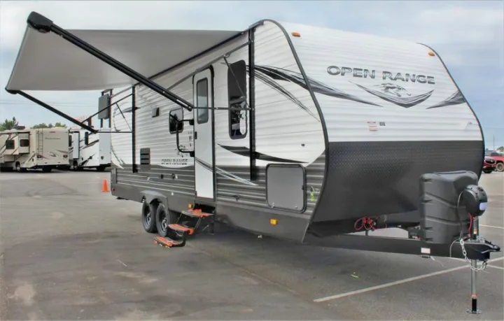 An Open Range travel trailer with an extended awning and front hitch, ideal for rv rental, parked on asphalt.. Open Range 26BHS 2021