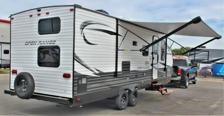 A white 'Open Range' travel trailer, ready for adventure as an RV rental, features an extended awning, spare tire, and dual axles.. Open Range 26BHS 2021