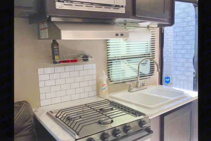 Modern RV rental kitchen with a stove, double sink, microwave, white subway tile, and window. Compact & functional.. Dutchmen Kodiak Express 2016