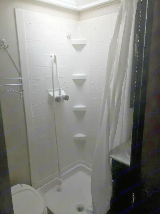 Compact RV rental bathroom with white tiled shower, multiple shelves, toilet, and towel rack. Brightly lit.. Dutchmen Kodiak Express 2016