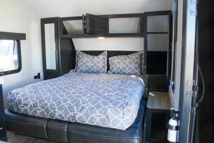 Cozy RV rental bedroom with gray patterned bedding, black cabinetry, and a window. Includes a fire extinguisher.. Forest River Cherokee Grey Wolf 2021