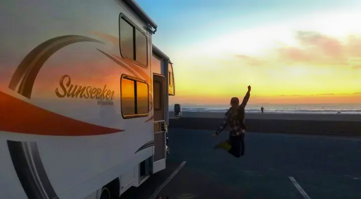 Sunset adventures: A person jumps with joy next to their Sunseeker rv rental by the ocean at dusk.. Forest River Sunseeker 2015
