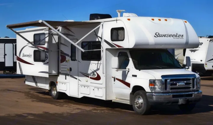 White Class C Sunseeker RV rental, built on a Ford chassis, with its awning and slide-outs extended, parked outdoors.. Forest River Sunseeker 2015