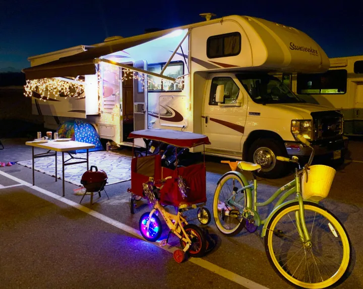 Nighttime RV rental setup: festive lights, outdoor mat, grill, child's tent, and bikes for an enjoyable camping trip.. Forest River Sunseeker 2015
