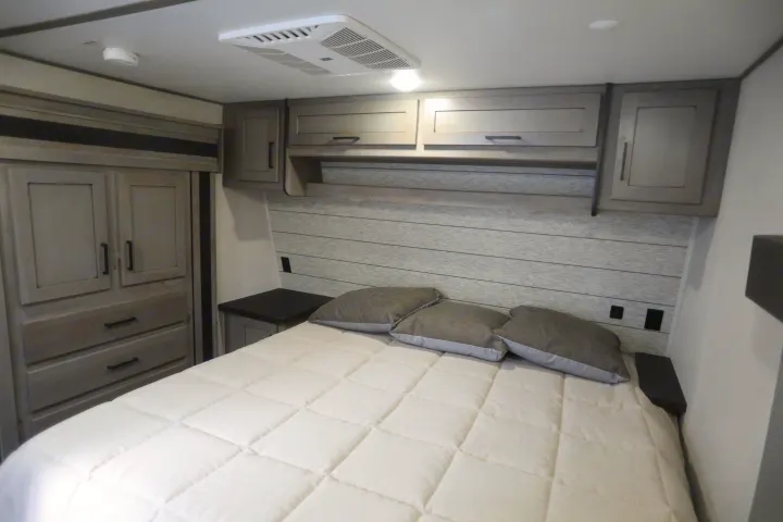 Cozy RV rental bedroom with a comfy bed, modern wood-look cabinets, and wardrobe storage for your travels.. Keystone Raptor 2020