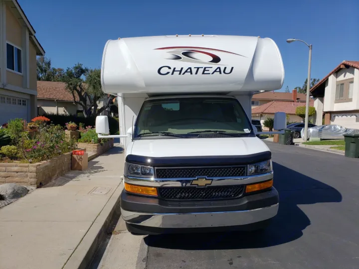 Front view of a white Chateau Class C rv rental parked in a neighborhood driveway on a clear day.. Thor Chateau 2021
