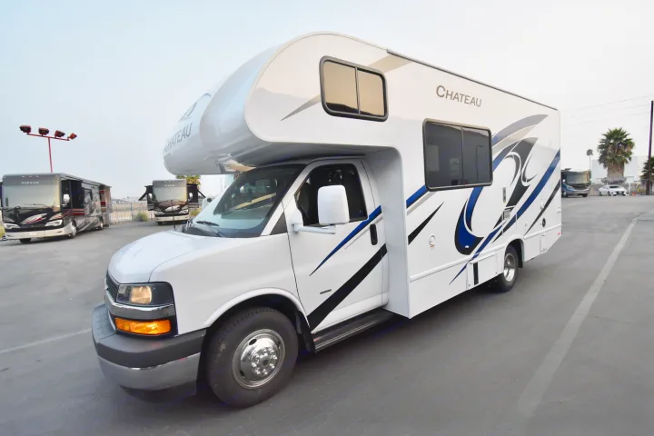 White Chateau RV rental, featuring blue and black graphics, parked on an outdoor lot with other RVs in the background.. Thor Chateau 2021