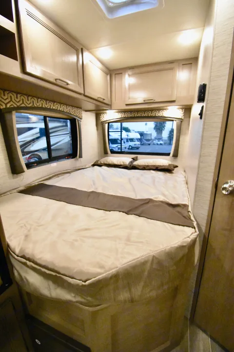 Explore a comfortable RV rental bedroom featuring a cozy bed, overhead storage, and scenic window views.. Thor Chateau 2021