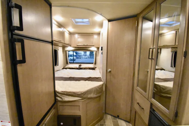 This RV rental bedroom offers a cozy bed, overhead storage, refrigerator, and mirrored closet. Ideal for travel.. Thor Chateau 2021