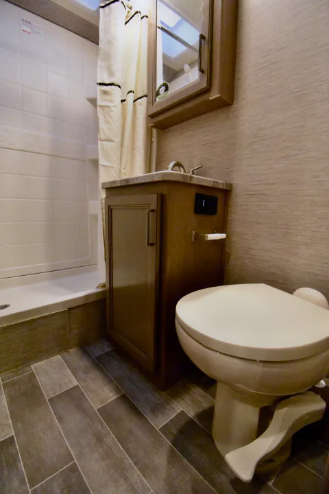 This compact RV rental bathroom features a small shower, vanity with sink, mirrored cabinet, and a foot-pedal toilet.. Thor Chateau 2021
