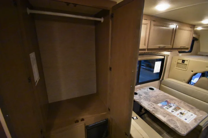RV rental interior with an open closet, hanging rod, overhead cabinets, and a dinette with bench seating.. Thor Chateau 2021