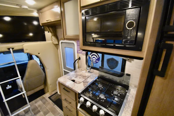 Discover this compact rv rental interior: A functional kitchen with a stove, sink, microwave, and TV for comfortable travel.. Thor Chateau 2021