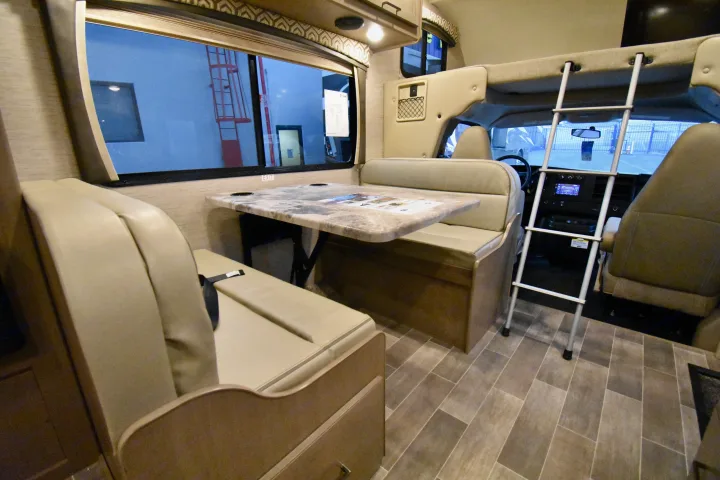 RV rental interior: dinette, overhead bunk with ladder, and driver's cabin. Features neutral tones and a tiled floor.. Thor Chateau 2021