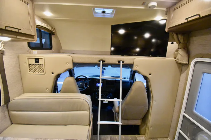Inside an rv rental: inviting dinette, cozy overhead bunk with ladder, and TV, overlooking the cab area.. Thor Chateau 2021