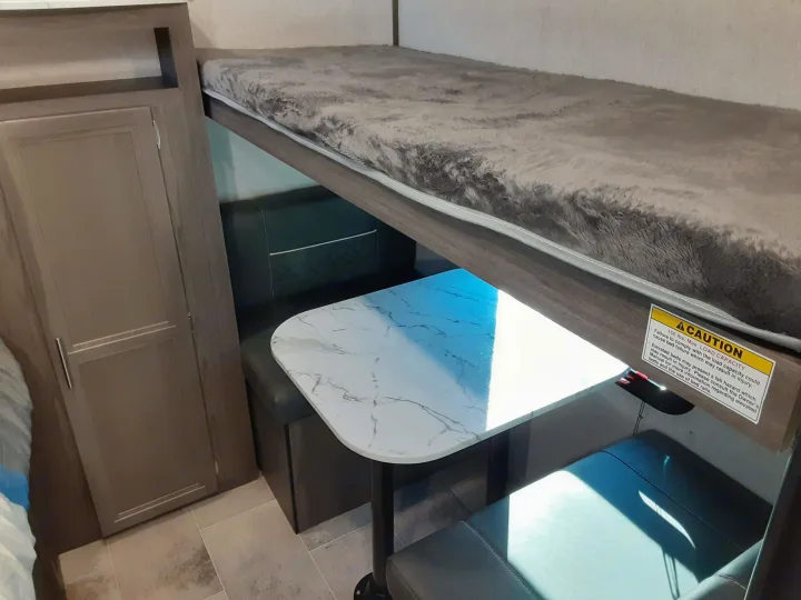 Compact RV rental interior featuring an upper bunk bed (150 lbs max.), dinette with table & seating, and storage.. Dutchmen Kodiak 2020