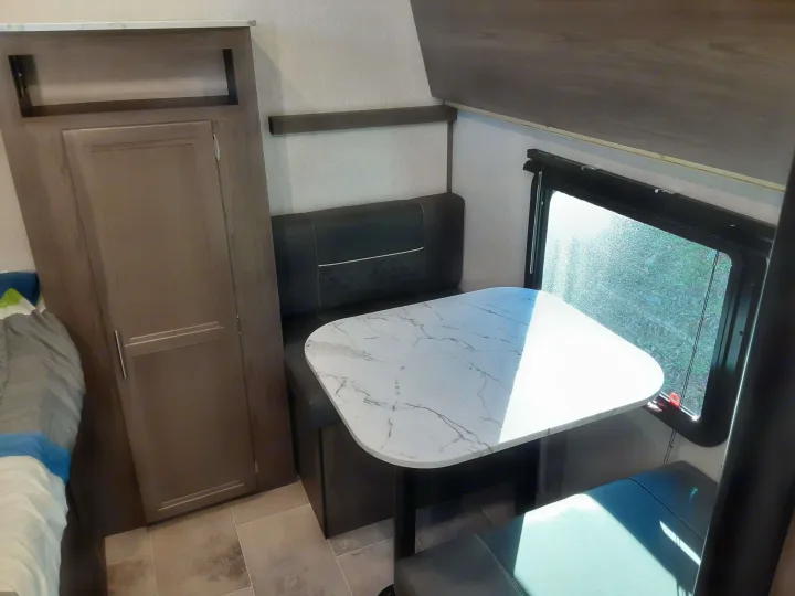 Inside an RV rental, featuring a dinette with a modern marble-top table, plush bench seating, and an adjacent storage cabinet.. Dutchmen Kodiak 2020