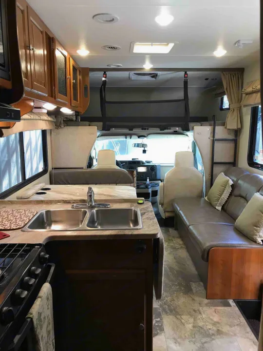 Explore this bright RV rental interior featuring a full kitchen, dining booth, comfy couch, and an overhead bunk with safety net.. Ford Coachman 2019