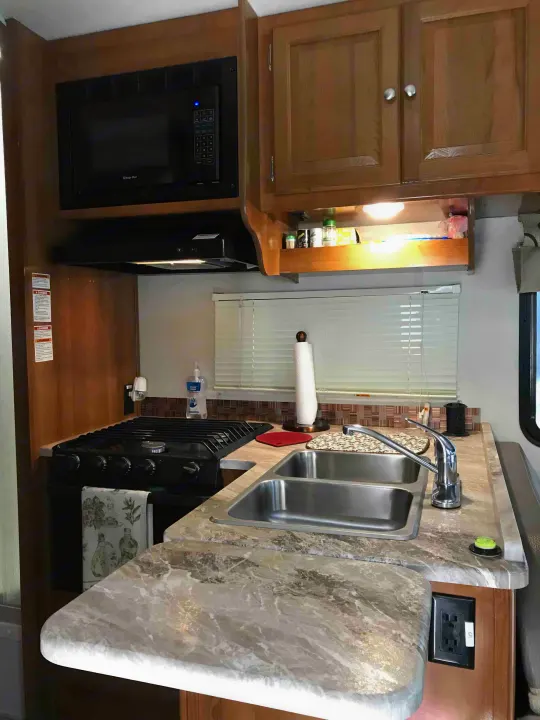 RV rental kitchen featuring an overhead microwave, gas stove, double sink, and marble-look countertops, ready for your trips.. Ford Coachman 2019