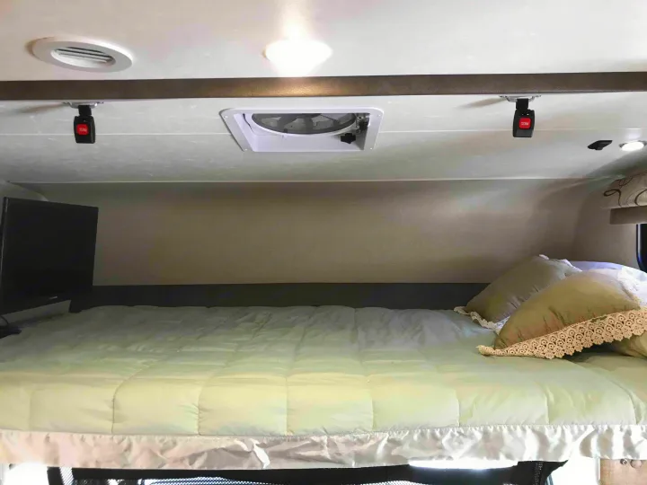 Cozy RV rental cab-over bunk with a bed, TV, overhead vent, and ceiling-mounted safety buckles.. Ford Coachman 2019