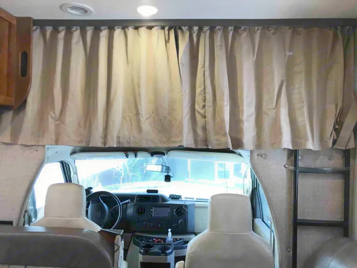 Inside an RV rental: The front cab area, with the dashboard and seats, is separated from the main cabin by drawn beige privacy curtains.. Ford Coachman 2019