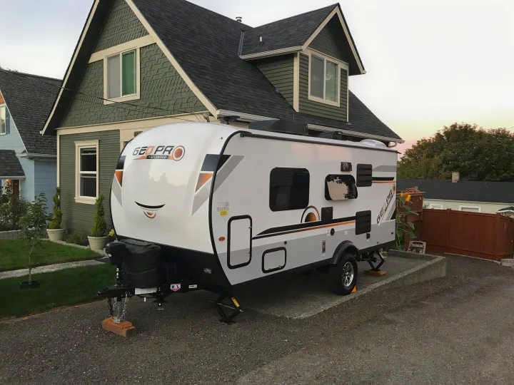 White Geo Pro travel trailer RV parked in a gravel driveway, ready for an RV rental adventure in front of a house.. Forest River Rockwood 2021