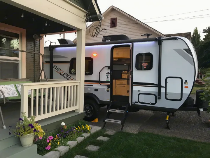 Bright Geo Pro RV rental with an open door revealing its interior, parked by a home's lit porch, ready for adventure.. Forest River Rockwood 2021