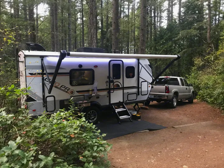RV rental trailer & pickup truck parked in a lush forest campsite, ready for outdoor adventures.. Forest River Rockwood 2021