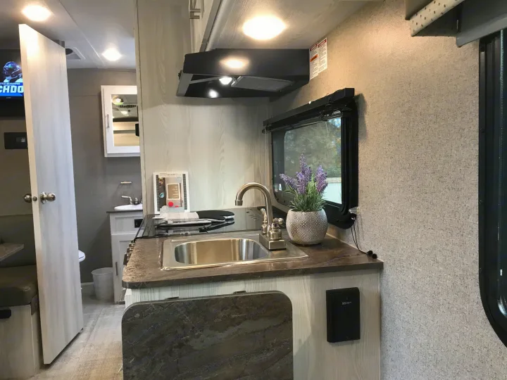 Modern RV rental kitchen with sink, cooktop, and window, showcasing a cozy interior and adjacent bathroom.. Forest River Rockwood 2021