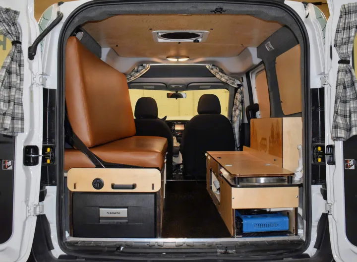 This RV rental campervan interior features a brown upholstered bed, Dometic fridge, and compact kitchen with sink and stove.. Dodge Promaster City 2019