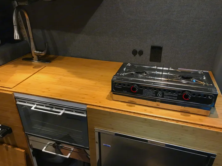 Modern RV rental kitchen with bamboo counter, sink, Dometic stove, oven, and Isotherm fridge for road trips.. Mercedes Benz Sprinter 2018