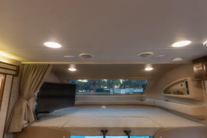 This RV rental offers a cozy, well-lit cab-over bunk with a mounted TV and window view, ideal for relaxing on the road.. Entegra Coach Esteem 31F 2021