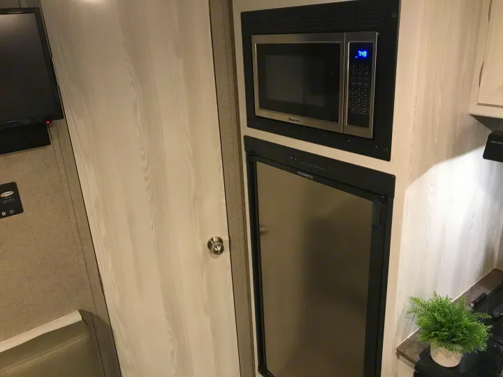 This RV rental interior features a compact kitchen with a Magic Chef microwave, Dometic refrigerator, and a wall-mounted TV.. Forest River Rockwood 2021