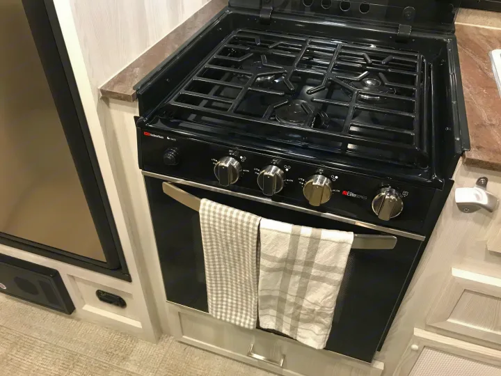 RV rental kitchen: a black Suburban stove/oven unit, four burners, control knobs, and two towels. Essential for on-the-go cooking.. Forest River Rockwood 2021
