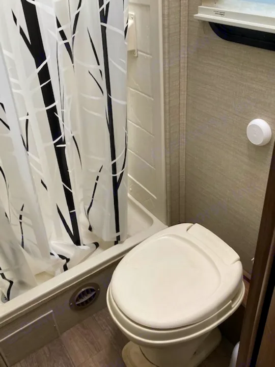RV rental bathroom interior shows a compact white toilet, shower with a black/white curtain, and ceiling safety alarm.. Jayco Redhawk 2018