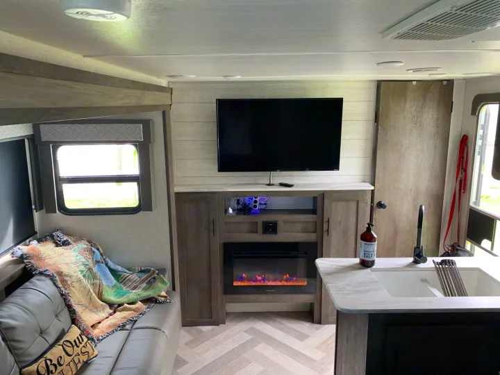 Cozy RV rental interior with a comfy couch, TV, electric fireplace, and kitchen sink, showcasing a modern living space.. Forest River Wildwood X-Lite 2020