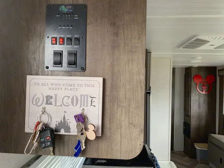 This RV rental's cozy interior features a control panel, a Disney-themed "Welcome" key holder, and Mickey Mouse decor.. Forest River Wildwood X-Lite 2020