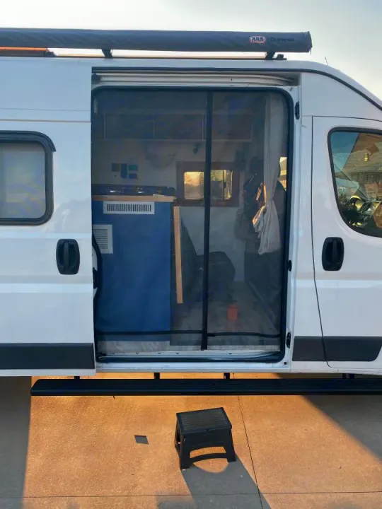 RV rental with open side door showing screen & custom interior, plus an awning. A step stool is outside.. Dodge RAM Promaster 2500 159' Wheelbase 2017