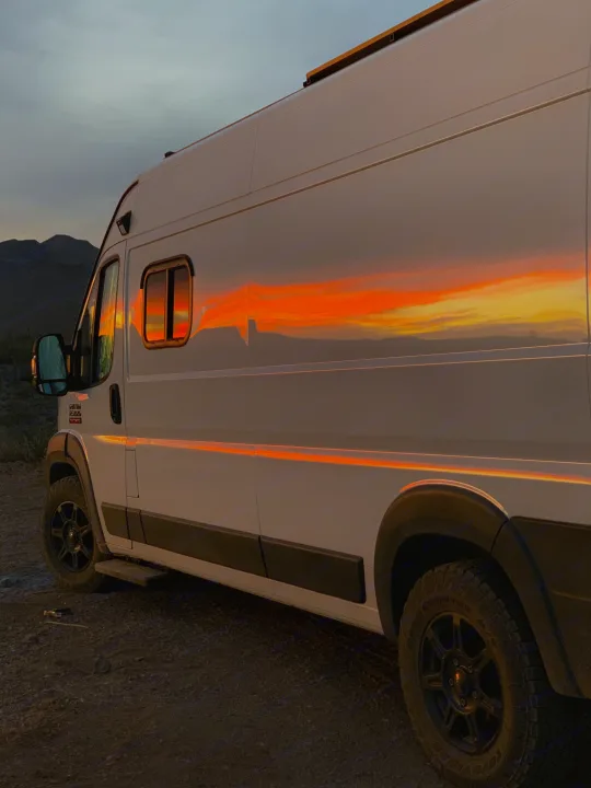 Stunning sunset reflecting vibrantly off a white RV rental, parked in a serene mountain desert.. Dodge RAM Promaster 2500 159' Wheelbase 2017