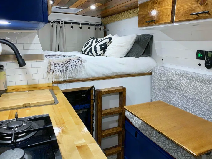 This cozy RV rental interior features a compact kitchen, elevated bed with a ladder, and a convertible dining area.. Dodge RAM Promaster 2500 159' Wheelbase 2017