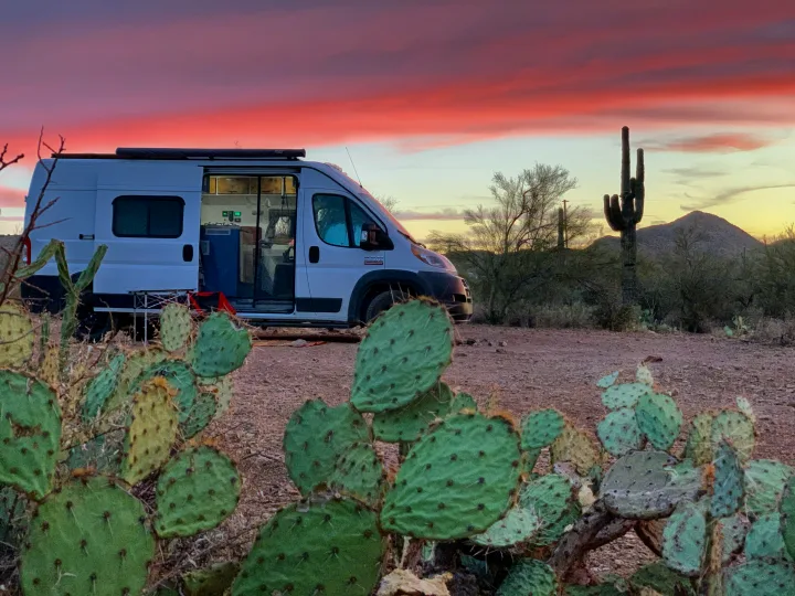 An RV rental parked in a vibrant desert sunset, surrounded by saguaro and prickly pear cacti, ideal for camping.. Dodge RAM Promaster 2500 159' Wheelbase 2017