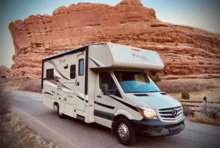 Scenic RV rental adventure: A beige Class C motorhome parked on a desert road with large red rock formations.. Coachmen Prism 2016