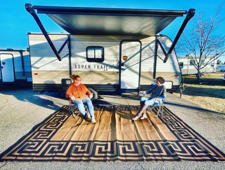 Enjoying an RV rental! Two people relaxing by their travel trailer under an awning on an outdoor rug. Camping fun!. Aspen Other 2021
